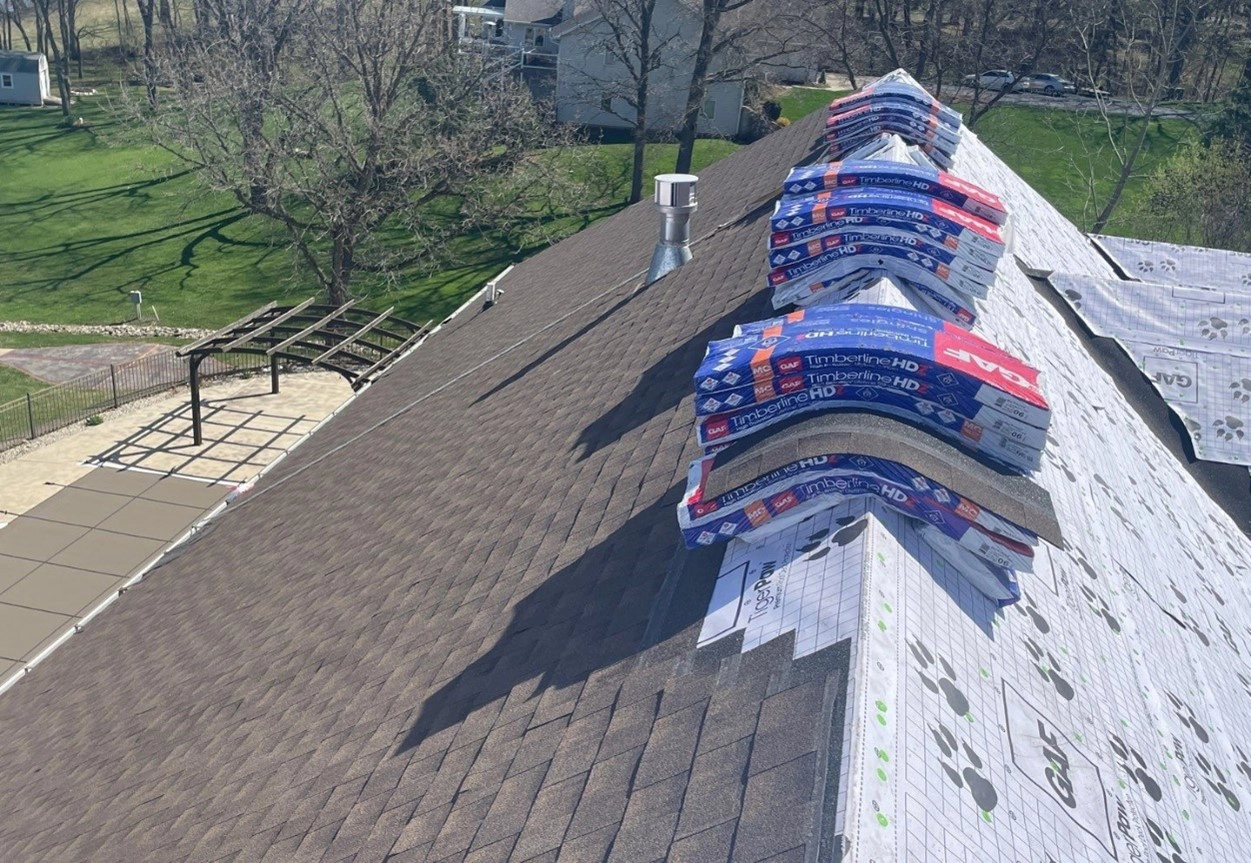 This is picture of a roof being installed by Sutton’s with packages of shingles laying over the ridge. The right side of the roof shows Tiger Paw underlayment.