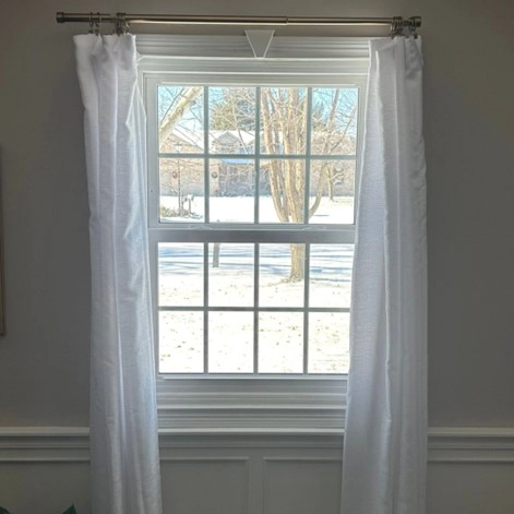 This is a photo of a window in a house in Springfield, IL with white curtains during the winter.