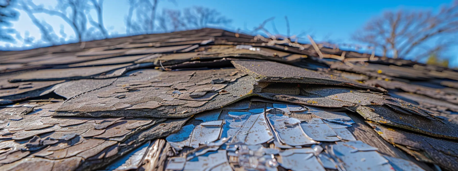 a close-up view of a weathered, shingled roof under a bright blue sky, showcasing contrasting sections of damaged and pristine shingles to illustrate the need for repair or replacement.